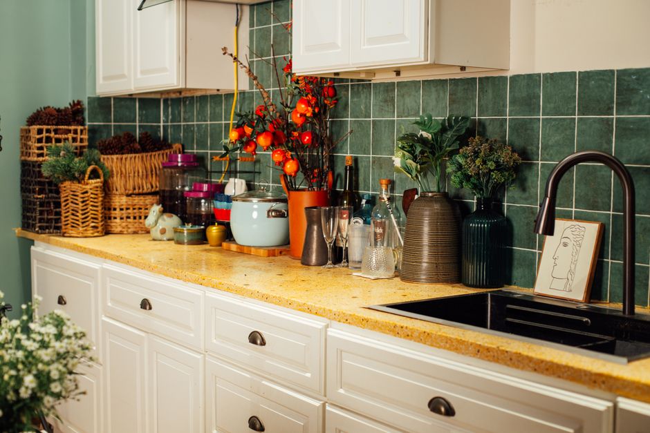 A charming kitchen countertop adorned with flowers, vases, and wicker baskets against vibrant green tiles.